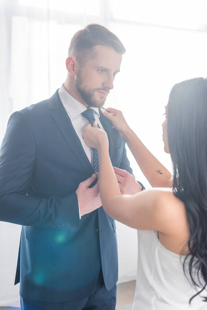 brunette woman touching tie of handsome bearded man in suit  - Фото, изображение