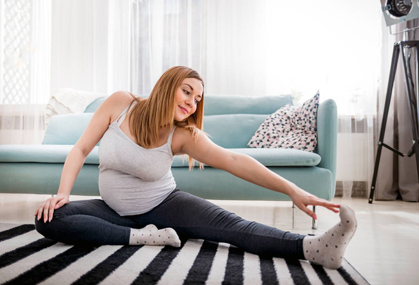 Beautiful pregnant woman doing exercise at home in living room, health during pregnancy - Foto, Bild