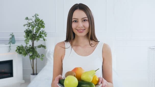 Portrait of attractive caucasian woman stretching out plate with fruits to the camera. - Video