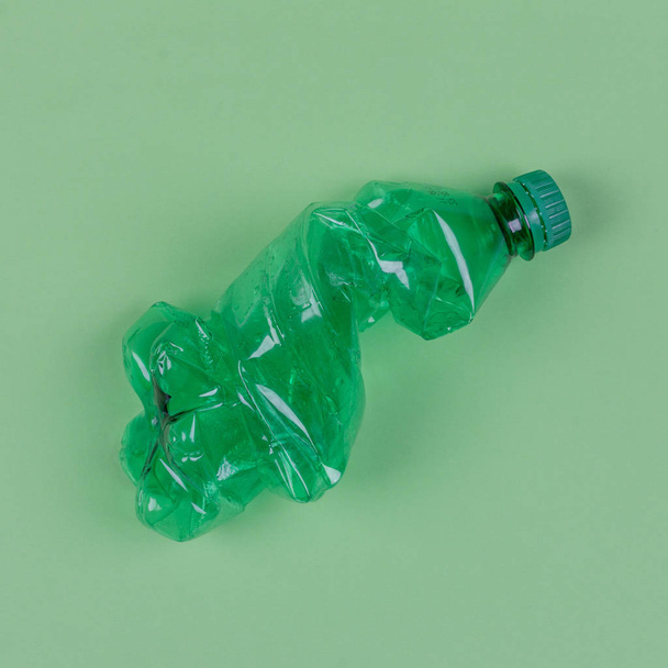 a green plastic bottle on a pale green background, top view. the concept of the problem to ban the use of plastic bags and containers and environment pollution - Photo, Image