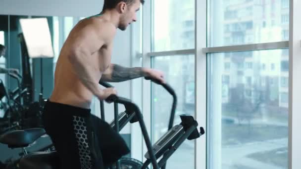 Young man wearing training hardly on cycling machine - Imágenes, Vídeo