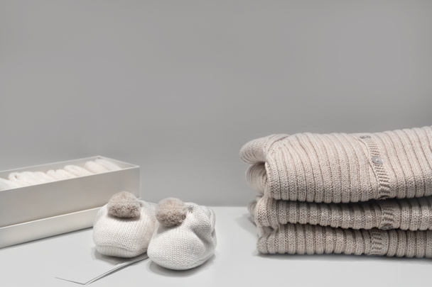 Botines de bebé, suéteres y calcetines hechos de telas beige natural se encuentran sobre la mesa
. - Foto, imagen