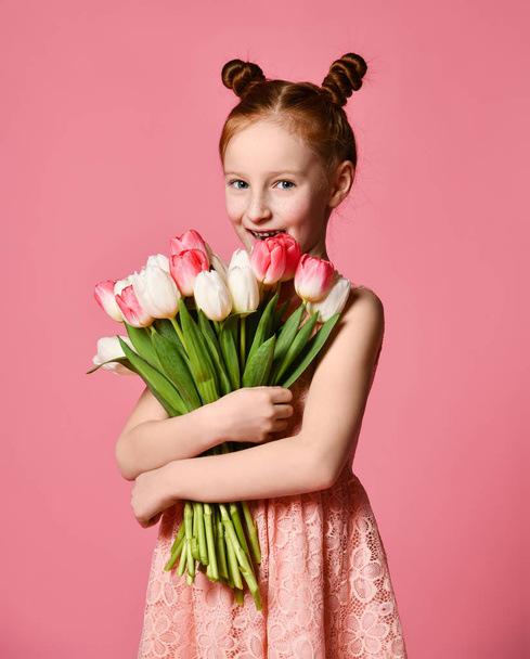 Portret van een mooi jong meisje in jurk houden grote boeket van irissen en tulpen geïsoleerd op roze achtergrond - Foto, afbeelding