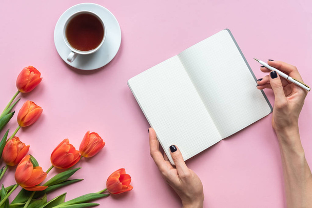 Notebook csésze tea és női kéz rózsaszín háttér. Lemezterület másolása - Fotó, kép