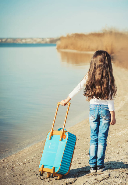 Nettes kleines Mädchen mit Koffer am Strand. Sommerzeit-Konzept. - Foto, Bild
