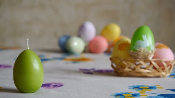 Mano femminile mettendo sul tavolo tre candele pasquali. Verde, arancione e giallo. Uova di Pasqua colorate sullo sfondo
. - Filmati, video