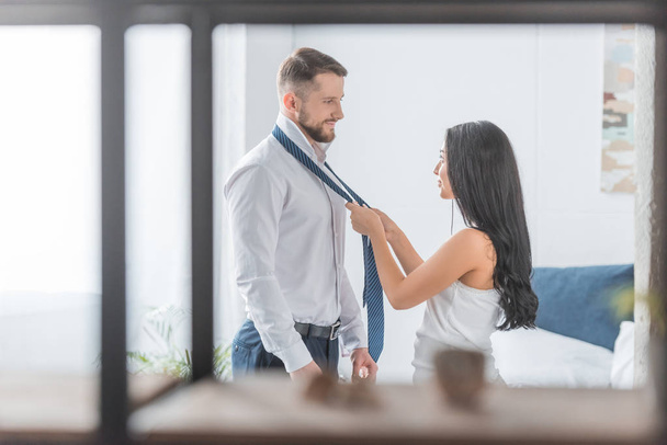 selective focus of beautiful brunette woman tying tie on bearded man at home  - Foto, Imagem