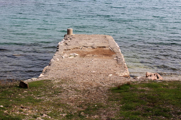 Stone pier surrounded with sea with small waves, uncut grass and small stones on windy winter day - Foto, Imagen