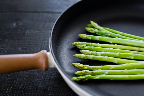 Fresh organic asparagus in a frying pan. Black background, top view, space for text. - Fotó, kép