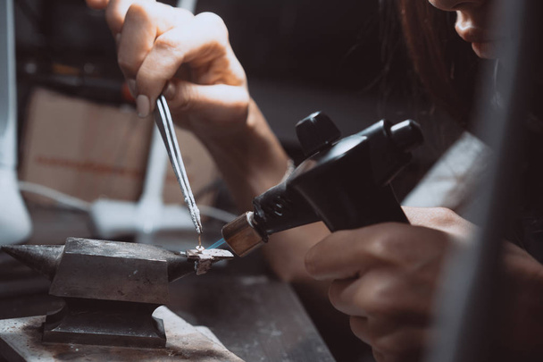 En el taller, una joyera mujer está ocupada soldando joyas
 - Foto, imagen