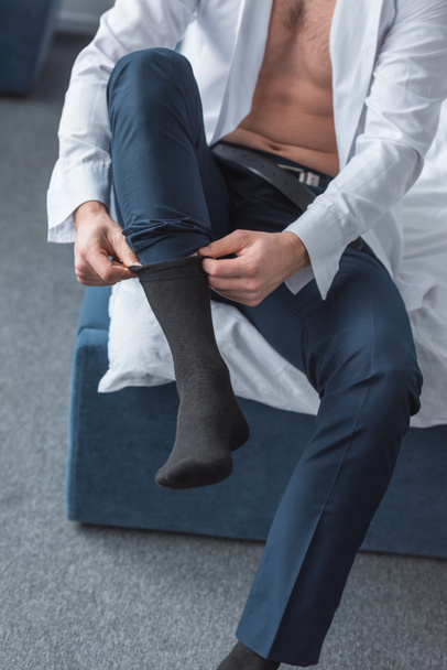 cropped view of man sitting on bed and wearing black socks in bedroom  - Foto, Imagem