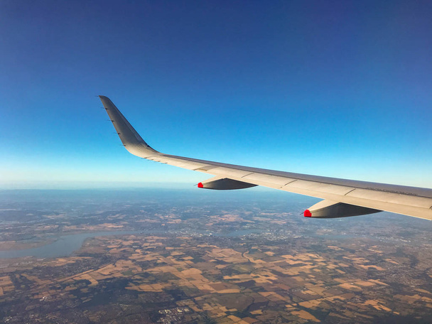 IN FLIGHT OVER EUROPE - AGOSTO 2018: Ala de uma aeronave em voo com céu azul e padrão de campos abaixo
 - Foto, Imagem