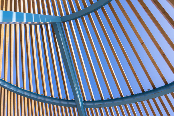Architecturale halfronde constructie van een blauwe, reeds licht verroeste metalen frame en houten latten met open ontwerp - Foto, afbeelding