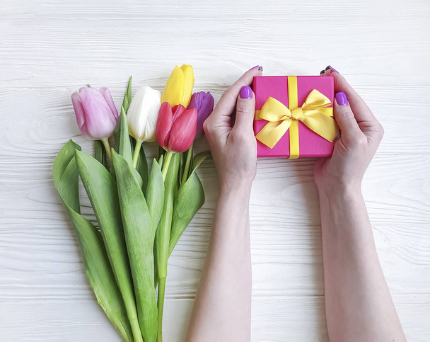 kobiece ręce trzymanie pudełka na prezent, bukiet tulipany na drewnianym tle - Zdjęcie, obraz