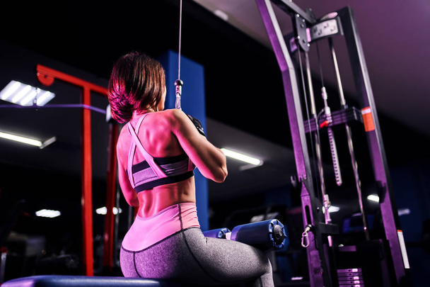 Athletic woman doing exercise for back, using machine, in gym - back view - Valokuva, kuva