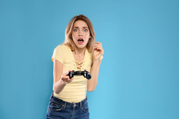 Emotional young woman playing video games with controller on color background. Space for text - Foto, imagen