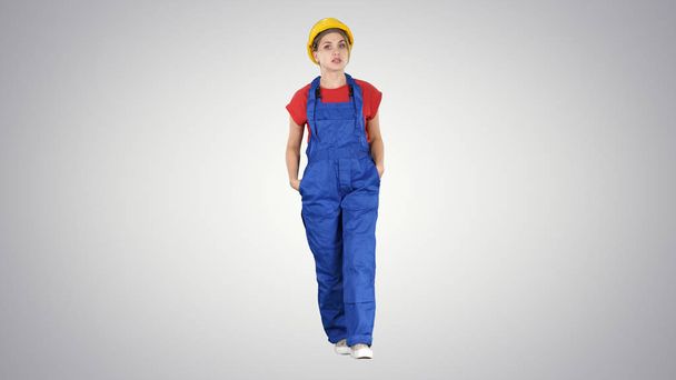 Woman builder with hands in pockets walking and telling a story to camera on gradient background. - Foto, immagini