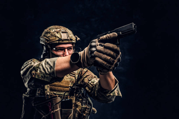 Foto de estúdio contra uma parede de textura escura. A unidade de elite, o soldado das forças especiais em uniforme de camuflagem com uma pistola e aponta para o alvo
 - Foto, Imagem