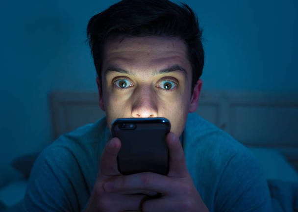 Young mobile phone addict man awake at night in bed using smartphone for chatting, flirting and sending text message. In communication, Internet addiction and Social media network abuse concept - Φωτογραφία, εικόνα
