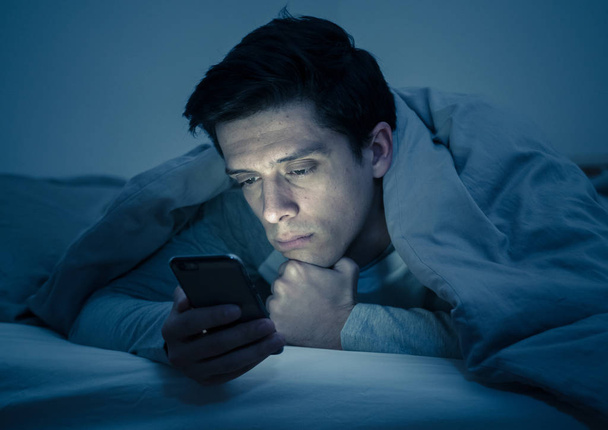 Young mobile phone addict man awake at night in bed using smartphone for chatting, flirting and sending text message. In communication, Internet addiction and Social media network abuse concept - Foto, Bild