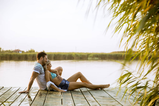 Loving couple sitting on the pier on lake at summer sunset - Φωτογραφία, εικόνα