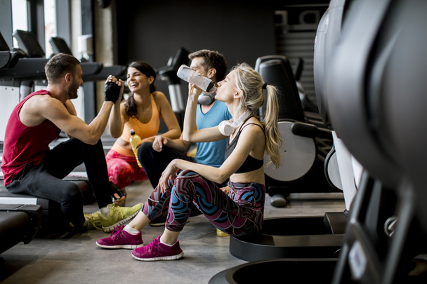Groupe de jeunes en vêtements de sport parlant et riant ensemble assis sur le sol d'une salle de gym après une séance d'entraînement
 - Photo, image