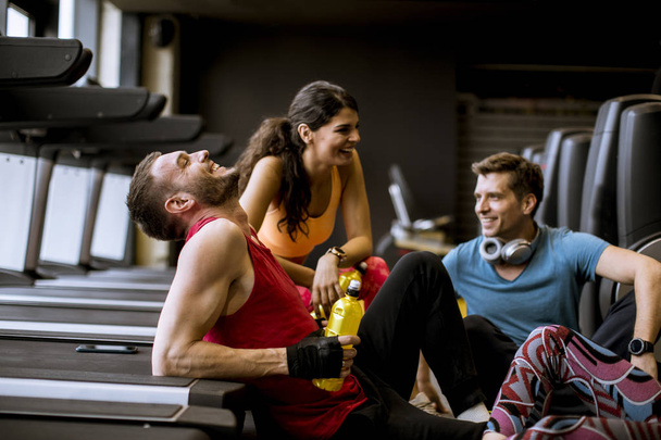 Grupa młodych ludzi w odzieży sportowej rozmawiając i śmiech razem siedząc na podłodze siłowni po treningu - Zdjęcie, obraz