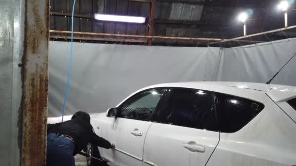 Russia, Moscow, April 2019: Brunette girl uses spray tool and covers car by froth in car-wash box. - Materiaali, video