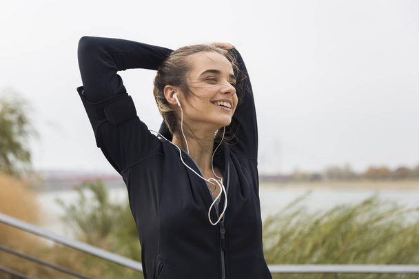 Mujer joven atleta estirando los brazos mientras escucha música al aire libre
 - Foto, imagen