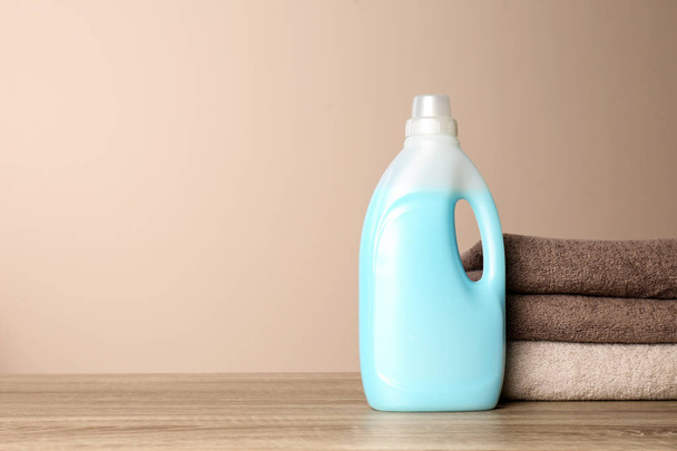 Bottle of detergent and clean towels on table against color background, space for text. Laundry day - Photo, image
