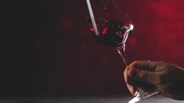abgeschnittene Aufnahme einer Person, die Rotwein im Glas auf dunkelrotem Hintergrund schüttelt - Filmmaterial, Video