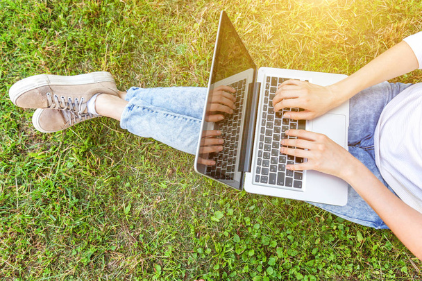 Woman legs on green grass lawn in city park, hands working on laptop pc computer. Freelance business concept - 写真・画像