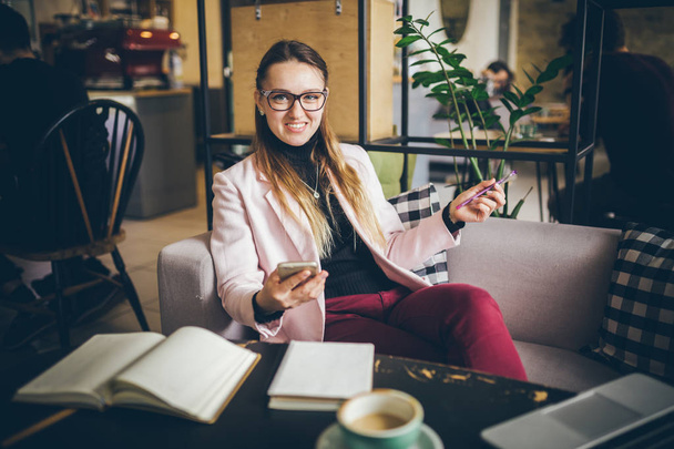 theme modern profession female blogger. Caucasian woman with glasses and jacket sitting inside coffee shop behind wooden table with notebook, laptop and cup coffee. Girl emotion dream, think writer - Photo, Image