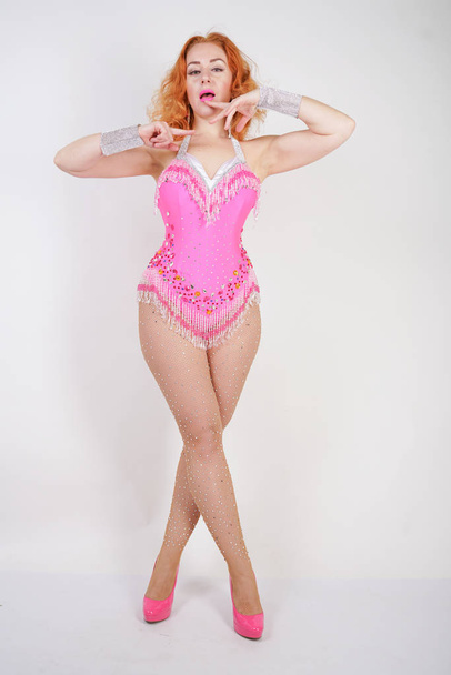 sexy red-haired caucasian girl in a pink bodysuit with tassels and  in fishnet pantyhose with rhinestone posing like a doll on a white background in Studio - Fotografie, Obrázek