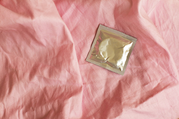 Condom on crumpled the pink bedsheet - Photo, image