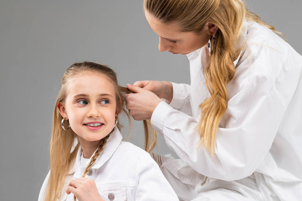 Attentive adult lady in white shirt collecting hair of her little sister - Photo, Image