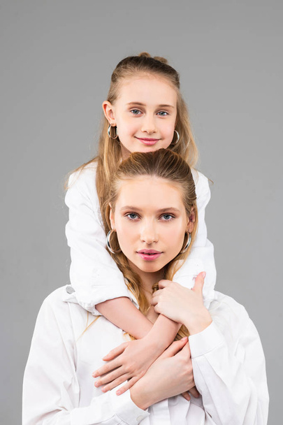 Smiling pleasant young kid with blue eyes leaning on her elder sister - Foto, Imagem