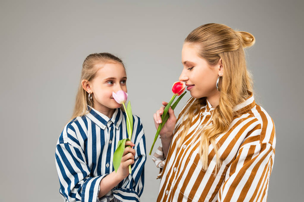 Pretty appealing girls with light hair smelling scent of first spring tulips - Фото, изображение