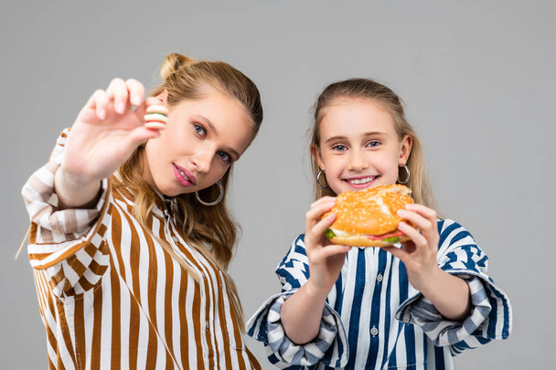 Cheerful young girls holding big burger in both hands - Фото, зображення