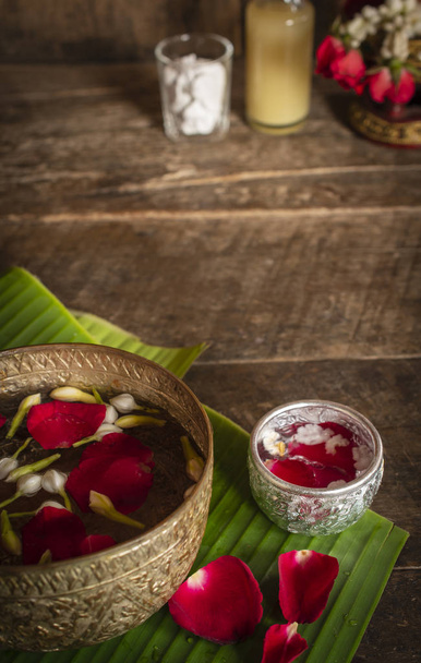 Red rose, Jasmine and popped rice on the calm water surface placed on the wood table Ready for pour water on the hands of revered elders and ask for blessing. - Photo, Image