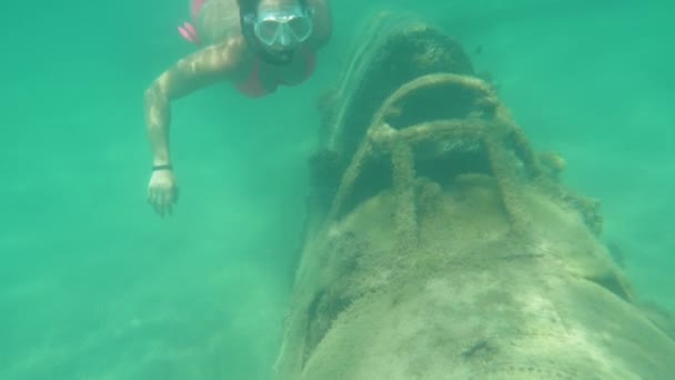 水中、スローモーション:若い女性シュノーケラーは奇妙にターコイズブルーの海の深い崩壊軍機のコックピットを見ています。女性旅行者は美しい海でダイビングで彼女の夏休を楽しんでいます. - 映像、動画