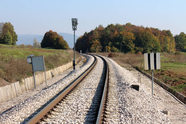 Pistas de ferrocarril curvas rodeadas de múltiples señales y luces de señales ferroviarias con grava y bosque denso sobre fondo de cielo azul claro
 - Foto, Imagen