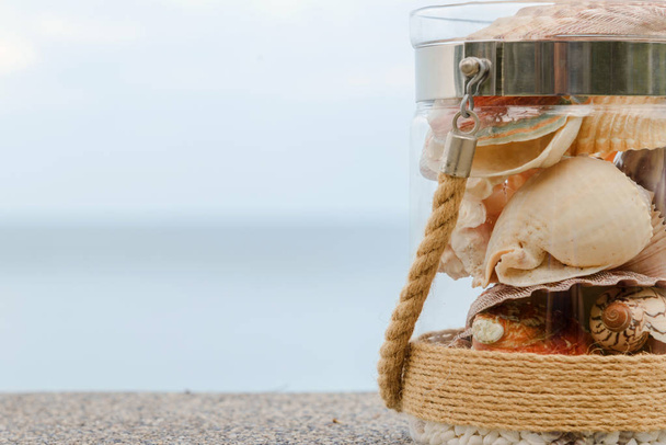 Variety of sea shells in glass jar and seascape on background with copy space. holiday concept - Foto, Imagem