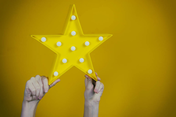beautiful toy in the shape of a star in the hands of a teenager on a yellow background - Foto, afbeelding