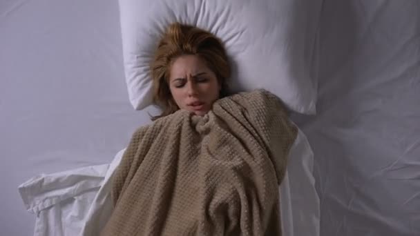 Woman covering with blanket lying in bed, feeling fever, symptoms of cold - Πλάνα, βίντεο