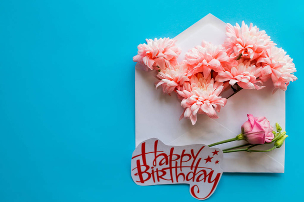 happy birthday card. opened craft paper envelope filled with spring blossom flowers. Top view, flat lay.greeting card with pink chrysanthemums on blue background.Birthday or happy event. - Fotografie, Obrázek