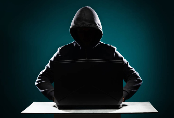 Porträt eines Computerhackers in Kapuzenpulli. verdunkeltes dunkles Gesicht. Datendieb, Internetbetrug, Darknet und Cyber-Sicherheitskonzept. - Foto, Bild