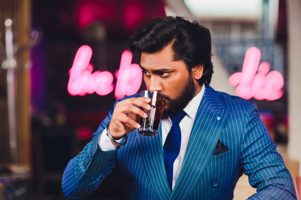 Handsome young man drinking cocktail at bar counter, wearing business suit. - Foto, imagen