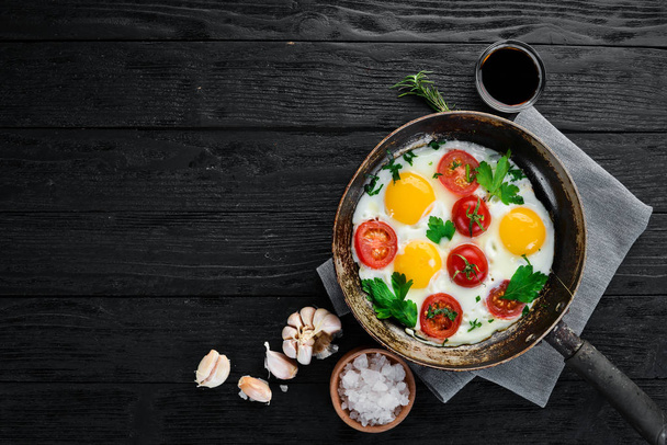 Eggs with tomatoes and greens in a frying pan. - 写真・画像