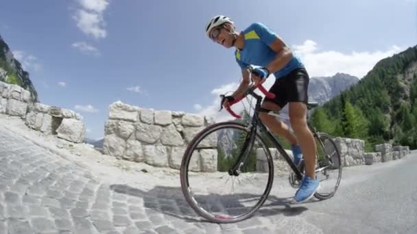 Спортивний молодий чоловік ступає на педалі свого крутого шосейного велосипеда під час інтенсивних гірських перегонів. Тренування велосипедистів по дорозі в сонячних горах. Мальовнича їзда на велосипеді в літній природі. Повільні кадри руху
 - Кадри, відео